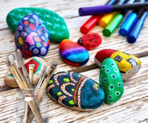 Assorted painted rocks next to paintbrushes and coloured pens 