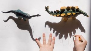 child drawing around dinosaur toys shadows - summer children's activity idea